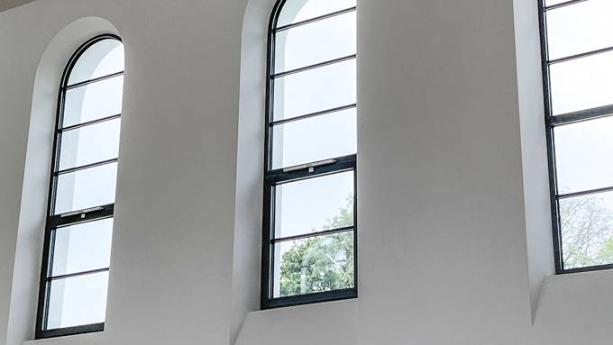 Three arched windows in a minimalist interior, letting in natural light and framed by clean white walls and a textured ceiling.