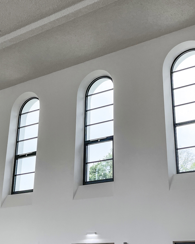 Three arched windows in a minimalist interior, letting in natural light and framed by clean white walls and a textured ceiling.