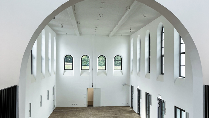 Spacious, modern hall with high ceilings and arched windows, featuring wooden flooring and natural light streaming in.
