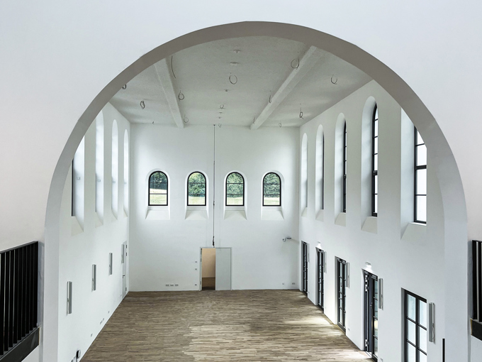 Spacious, modern hall with high ceilings and arched windows, featuring wooden flooring and natural light streaming in.