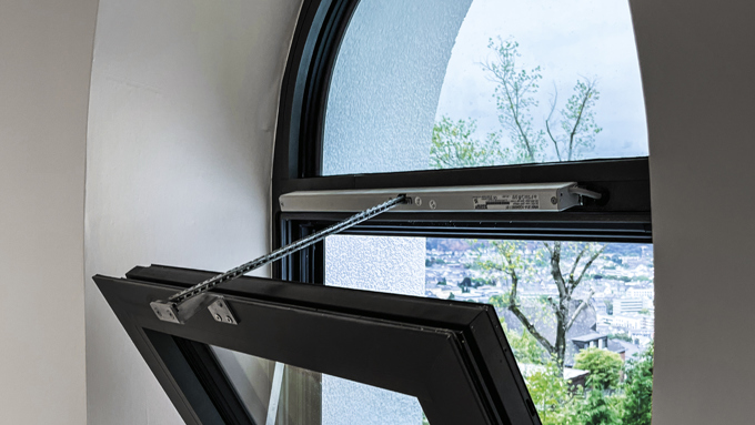 A modern arched window is ajar, revealing a view of greenery and a partially finished outdoor area beyond.