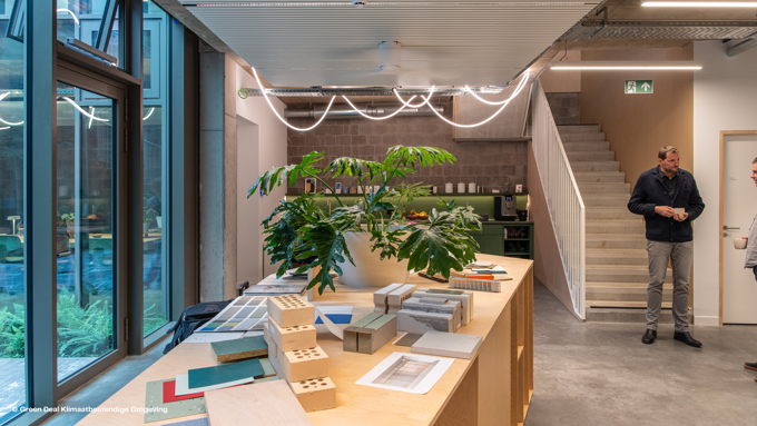 Bright, modern office space featuring a wooden table with design samples, plants, and an open staircase in the background.