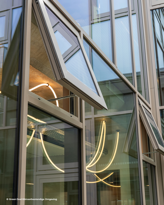 Modern building exterior with angular glass windows, some open, reflecting neon light and showcasing contemporary architectural design.