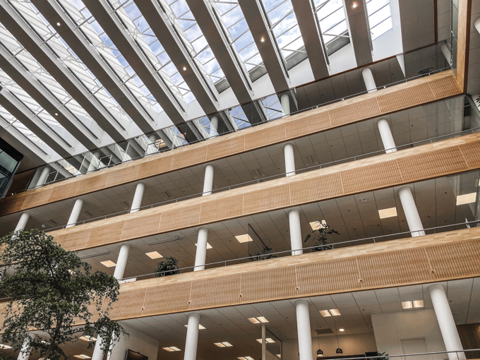 Interior view of a modern building with wooden panels, large glass skylights, and greenery on multiple levels.